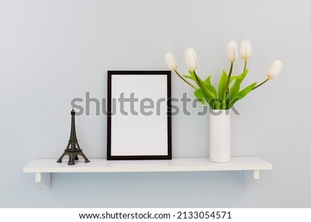 A black vertical frame stands on a shelf, next to the Eiffel Tower and tulips
