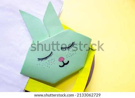 cute origami rabbit on a shooping paper pack or nest for eggs. easter holiday, greeting card. cute sleeping bunny. Do it yourself concept (DIY), activities for kids. instructions for art project.