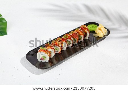 Maki sushi with salmon and teriyaki sauce on black plate. Maki roll with salmon tartare outside and tuna, cheese and cucumber inside. Sushi menu on white background with hard shadow and leaves