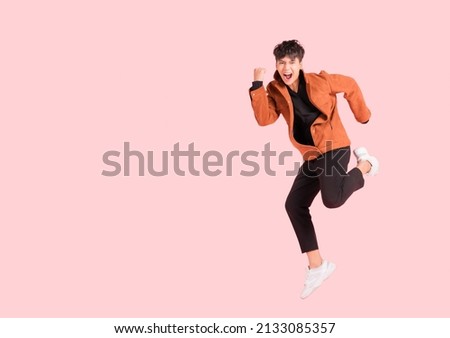 Happy handsome Asian man in fashionable clothing and jumping doing winner gesture isolated on pink background. Portrait of young male cheerful confident and excited jump in air and smile at studio. Royalty-Free Stock Photo #2133085357