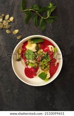 Vegan food. Breakfast oatmeal porridge with banana, strawberry sauce, pumpkin seeds and mint on a dark background in an eco paper box. Healthy balanced food. Top view, overhead, banner