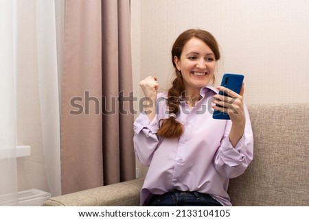 Happy red-haired girl with a smartphone in her hand. Young woman looks at the phone screen and rejoices. High quality photo