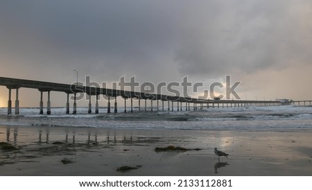 Ocean Beach pier in rainy weather, sea waves in foggy air, California coast, USA. Beachfront boardwalk on piles in water, San Diego. Misty cloudy dramatic shore under pouring downpour. Railfall drops. Royalty-Free Stock Photo #2133112881