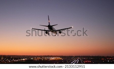 Airport runway lights at night, plane or airplane landing to airstrip, twilight dusk and sunset. Airliner jet arriving to aerodrome, San Diego airfield, California USA. Aircraft flying mid air in sky. Royalty-Free Stock Photo #2133112951