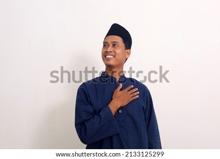 Portrait of happy asian male standing while holding his chest. He is feels relieved. Royalty-Free Stock Photo #2133125299