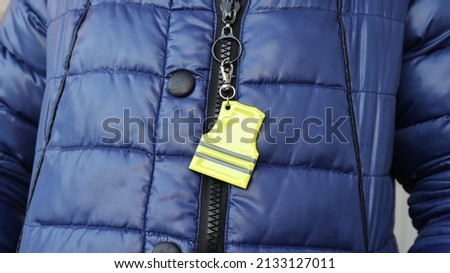 Elegant green reflective safety signal in a clothing pattern form on a blue winter warm clothes for pedestrian visibility. Accessory essential for a walker or passerby to walk on the dark street. Royalty-Free Stock Photo #2133127011