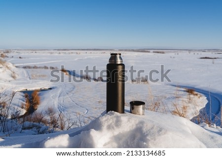 A black thermos on the background of a winter landscape. Camping equipment. High quality photo