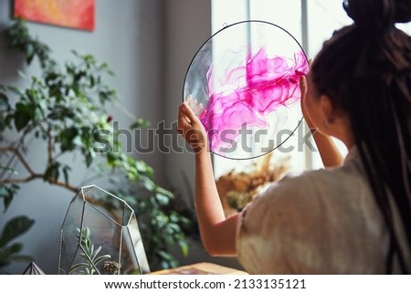 Dark-haired painter holding a round abstract picture before her