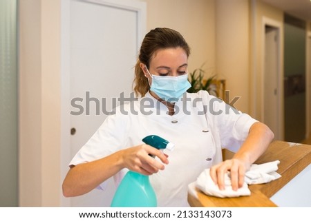 Woman in uniform cleaning reception desk of private clinic