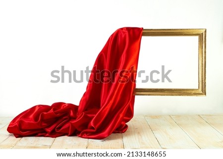 red satin cloth unveiling a golden frame. Levitating frame, mockup for presentation. Royalty-Free Stock Photo #2133148655