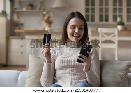 Happy young woman holds smartphone and credit card make purchase remotely, buy goods on internet, transfer money successfully use electronic services. E-shopping, secure pay through e-bank app concept Royalty-Free Stock Photo #2133148979