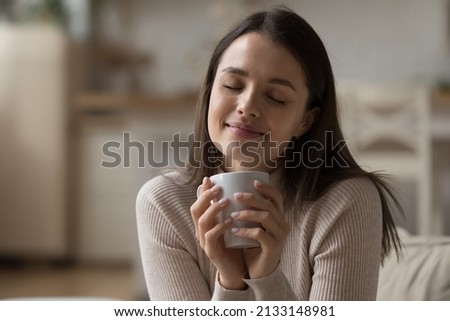 Close up beautiful woman relaxing on sofa with eyes closed, hold tea cup, take break at home enjoy favourite beverage looks carefree, relish aroma of coffee, daydreams alone indoor. No stress concept Royalty-Free Stock Photo #2133148981
