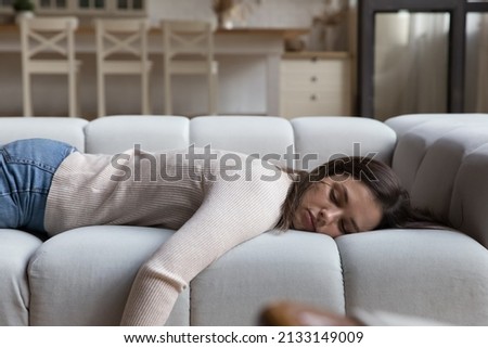 Tired woman have day nap on sofa. Unmotivated female lying at home alone in living room, feels mental or physical exhaustion, looking melancholic. Lack of energy after sleepless night, fatigue concept Royalty-Free Stock Photo #2133149009
