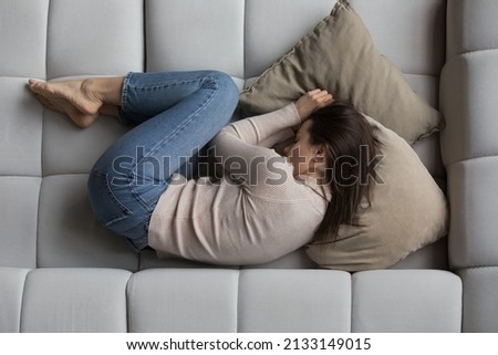 Top overhead view young peaceful woman lying on sofa at home. Female feels sick, suffers from illness or depression, thinking about personal problems, looking lonely. Daytime nap, life concern concept Royalty-Free Stock Photo #2133149015