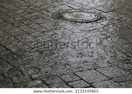 rainy puddle on the road and a drain in the back, rainy summer day in the city