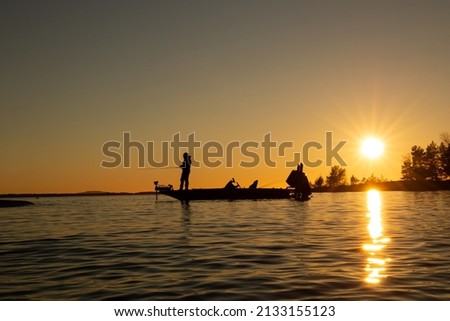 Pike fishing in the sunset with high speed bass boat. Lake Vänern in  Sweden. Angler casting with fishing rod, warm and orange glowing sky. Royalty-Free Stock Photo #2133155123