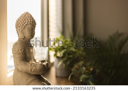 Zen spiritual ritual meditating white face of Buddha, brown candle on green floral background. Religion concept, esoterics. Still life style. Home decor. Place for text, copy space.Spiritual awakening