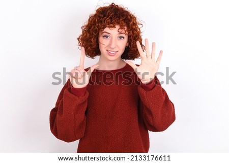 young redhead girl wearing red sweater over white background showing and pointing up with fingers number seven while smiling confident and happy.