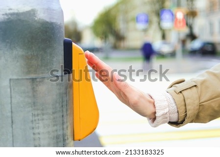 Close-up of a girl's hand in front of a traffic light switch at a pedestrian crossing