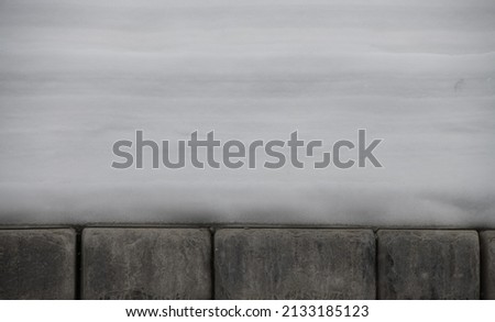 snow build up on top of rectangular cement or concrete brick shaped blocks on bottom snow layers built up over winter snow fall accumulation horizontal seasonal winter backdrop background or wallpaper Royalty-Free Stock Photo #2133185123