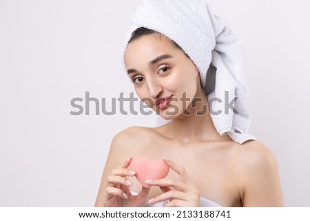 Beautiful girl with thick eyebrows and perfect skin at white background, towel on head, beauty photo. Holding a cosmetic pink heart sponge.