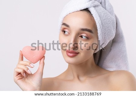 Beautiful girl with thick eyebrows and perfect skin at white background, towel on head, beauty photo. Holding a cosmetic pink heart sponge.