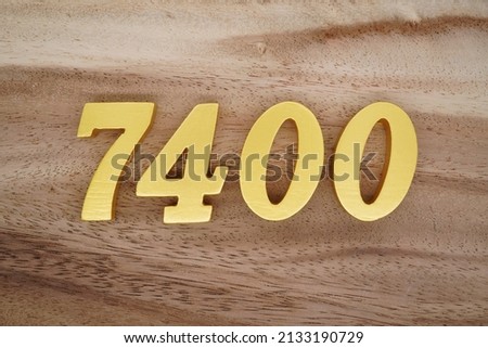Wooden  numerals 7400 painted in gold on a dark brown and white patterned plank background.