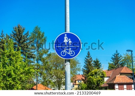 A pedestrian bicycle zone sign in a blue circle on background of green trees