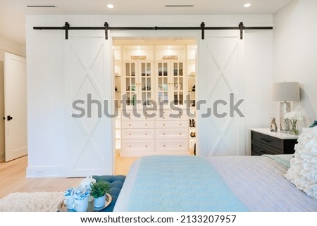 Master walk in closet and bedroom in white with glass cabinets blue accents and barn doors Royalty-Free Stock Photo #2133207957