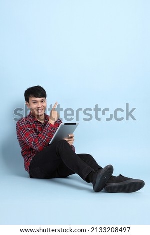 The young adult Asian man sitting on the blue background.