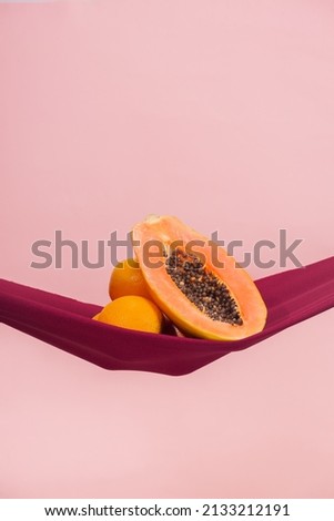 two oranges and a papaya cut in half on a red cloth in front of a peach background as a symbol of the pelvic floor, no people Royalty-Free Stock Photo #2133212191