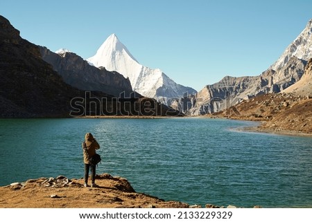 rear view of an asian photographer taking a photo of the holy mount jampayang and lake boyongcuo in yading national park, daocheng county, sichuan province, china