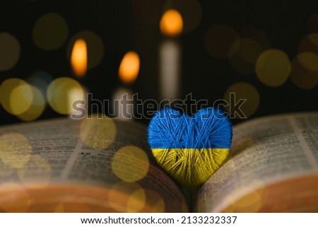 Yellow and blue heart and bible on a table by candlelight. Pray for Ukraine in the colors of the flag. Crisis in international relations, Russian military invasion of Ukraine.Pray Ukraine


