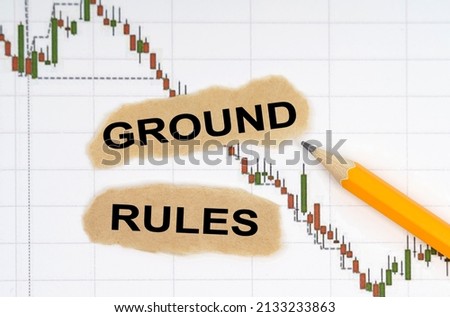 Finance and economy concept. On the table with charts of quotes are a pencil and pieces of paper with the inscription - GROUND RULES