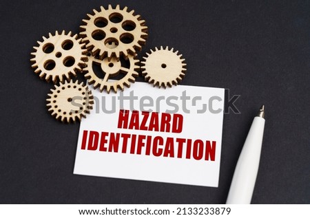 Industrial concept. On the black surface are gears, a pen and a business card with the inscription - Hazard Identification