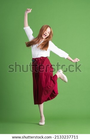 Beautiful young Asian woman dancing and posing on green background