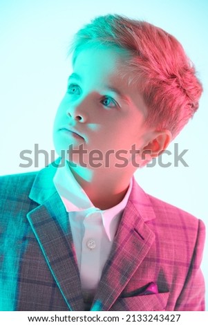 Children's fashion. Portrait of a handsome boy in a stylish suit posing on a light blue background in mixed pink and blue light. Smart casual style. Education. Studio shot.
