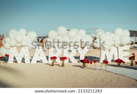 The sign of Marry me in big letters with roses on a beach Royalty-Free Stock Photo #2133251283