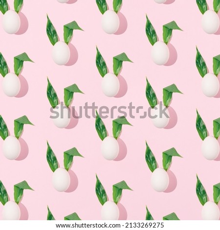 Easter abstract pattern made of white eggs with fresh green leaves as bunny ears on bright pink background. Minimal spring holiday concept. Creative surreal layout with sunshine shadow.