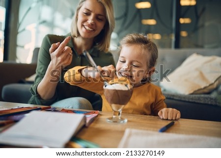 Mischief little girl having fun with whipped cream while eating mousse with her mother at home. Royalty-Free Stock Photo #2133270149