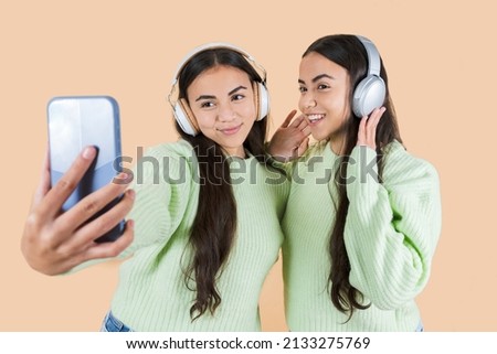 two women twin sisters listen to music and take a photo with a mobile phone with a camera