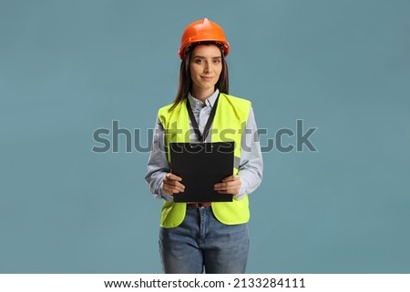 Young female engineer with a safety vest and hardhat holding a clipboard isolated on blue background Royalty-Free Stock Photo #2133284111