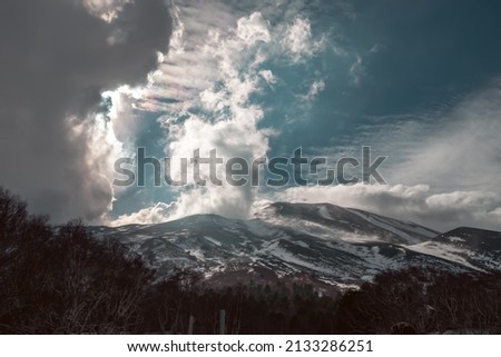 snowy volcano with forest and clouds