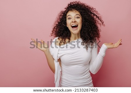 Happy young caucasian woman with wonderful sense of humor laughs mouth wide open on pink background. Dark-haired beauty in white blouse waves her arms. Mood, lifestyle, concept.