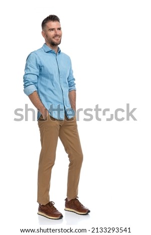 full body picture of bearded middle aged guy in casual outfit smiling and holding hands in pockets while looking away on white background in studio