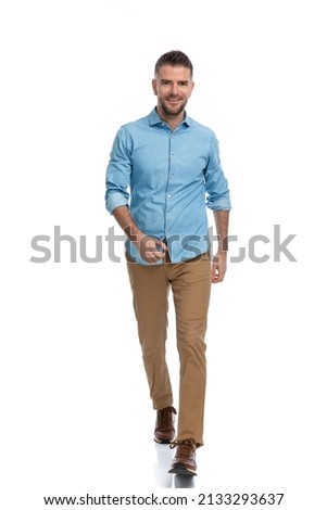 full body picture of confident unshaved man in casual outfit on white background walking and smiling in studio