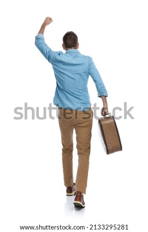 man with baggage holding fist in the air, celebrating freedom, running away and travelling around the world  Royalty-Free Stock Photo #2133295281