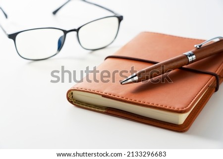 Leather notebook, pen and glasses placed on a white background. Business image.