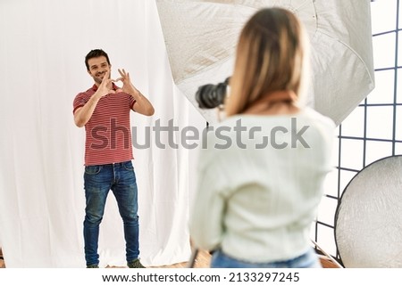 Woman photographer talking pictures of man posing as model at photography studio smiling in love showing heart symbol and shape with hands. romantic concept. 
