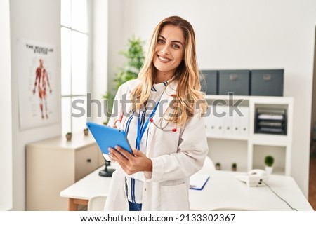 Young blonde woman wearing doctor uniform using touchpad at clinic